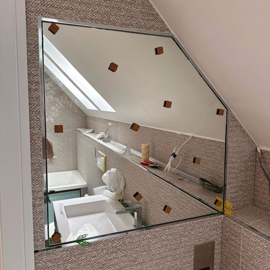 A bespoke shaped washroom mirror cut to fit flush with the sloping ceiling in this room